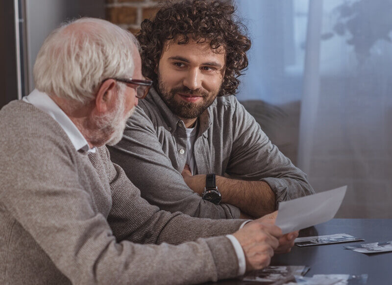 Adult son and senior dad holding old family photos.